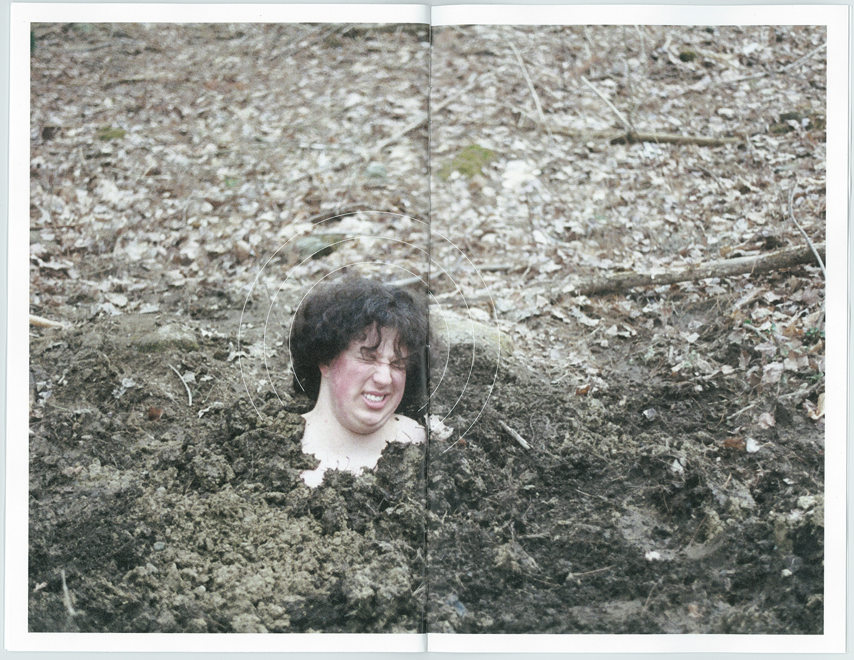 a man with curly dark brown hair is buried up to the neck in dirt. there are old, dried leaves surrounding him, he bears an expression of pain on his face. there is a set of concentric, thin, white arches surrounding his head, mirroring the style of halos from early bible paintings. the image itself is scanned out of printed book, the edges of the paper are visible around the edge of the image, along with there being a spine in the middle of the two-page spread.