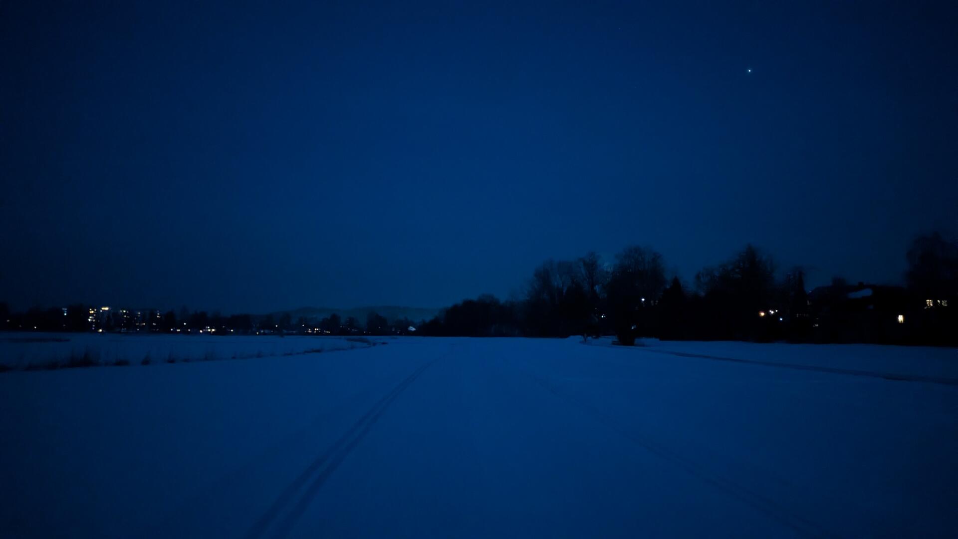 cross-country skiing tracks after sunset, rather blue tint. looking into the eastern sky. A lone visible star in the sky, and lights of some high-rises on the horizon.