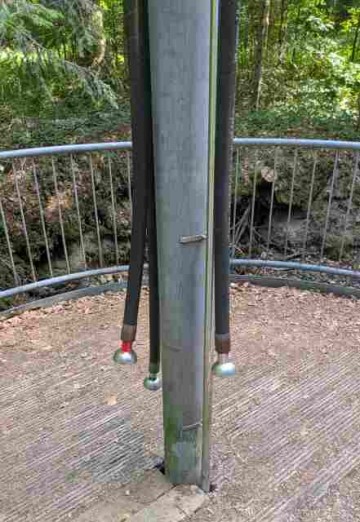 close up of a metal pillar in a forest on which tubes with funnels are attached.