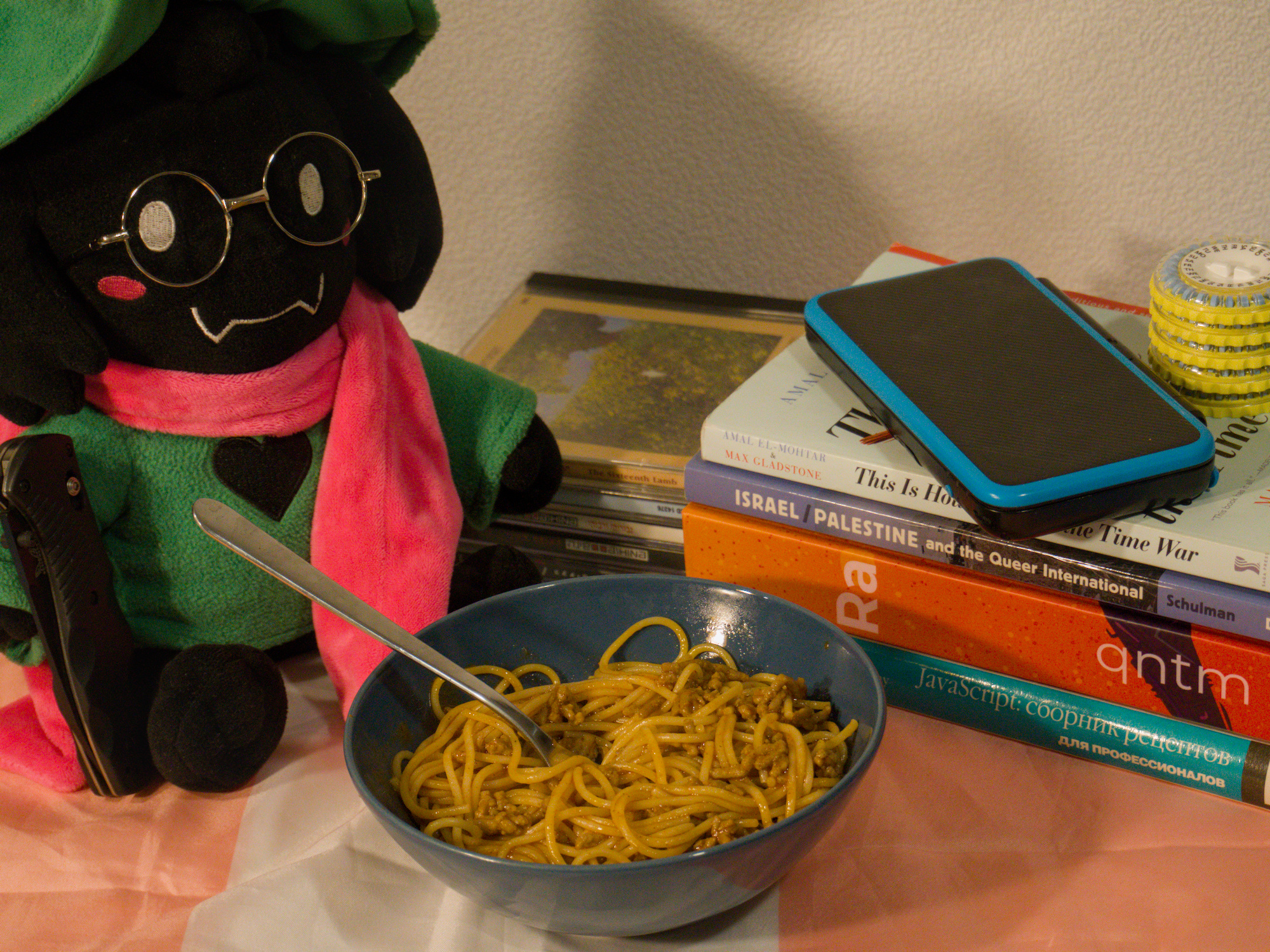 bowl of spaghetti bolognese. around it a ralsei plushie, some books, some cds, and a knife