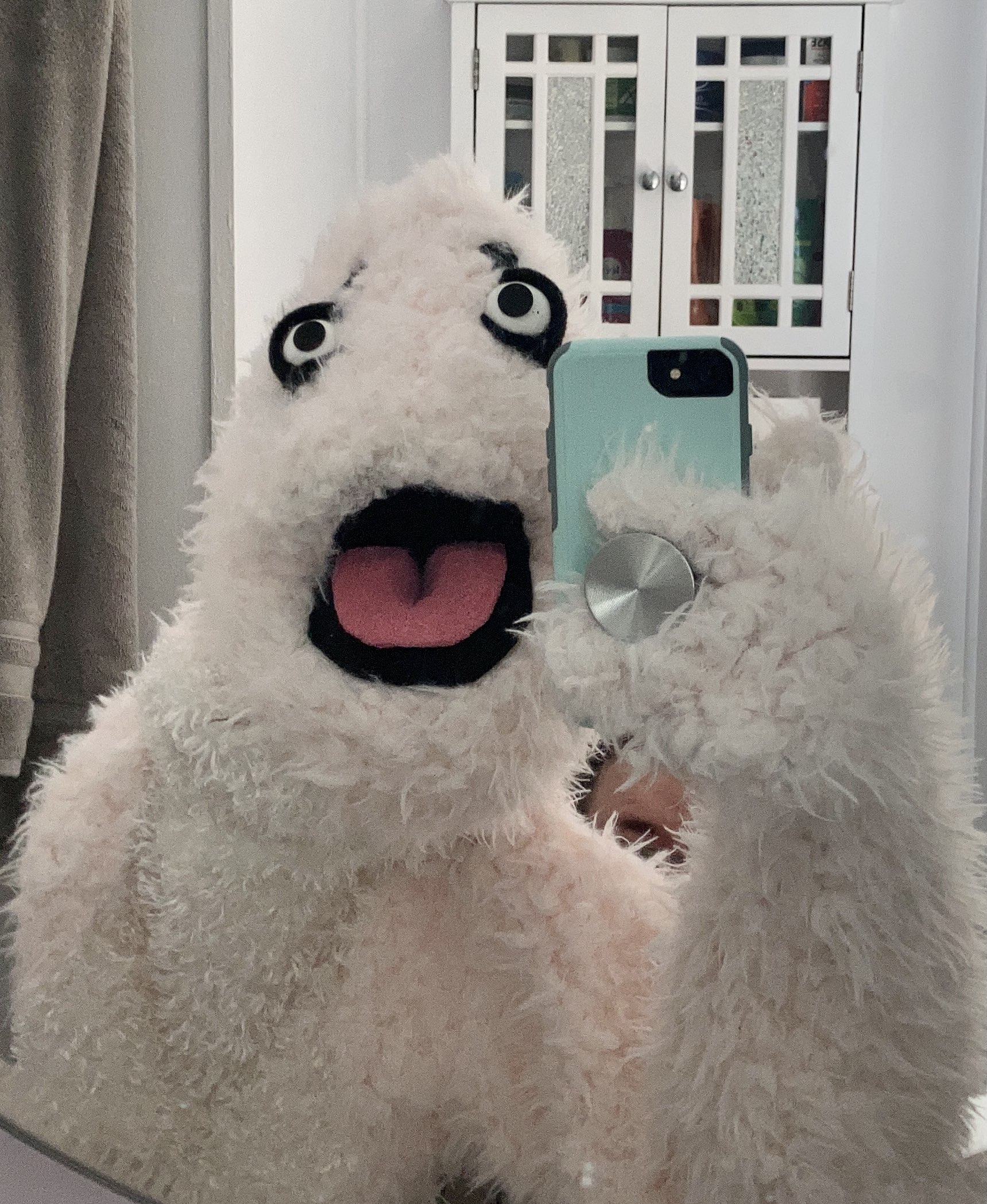 A human-sized pink muppet taking a selfie in a bathroom mirror.