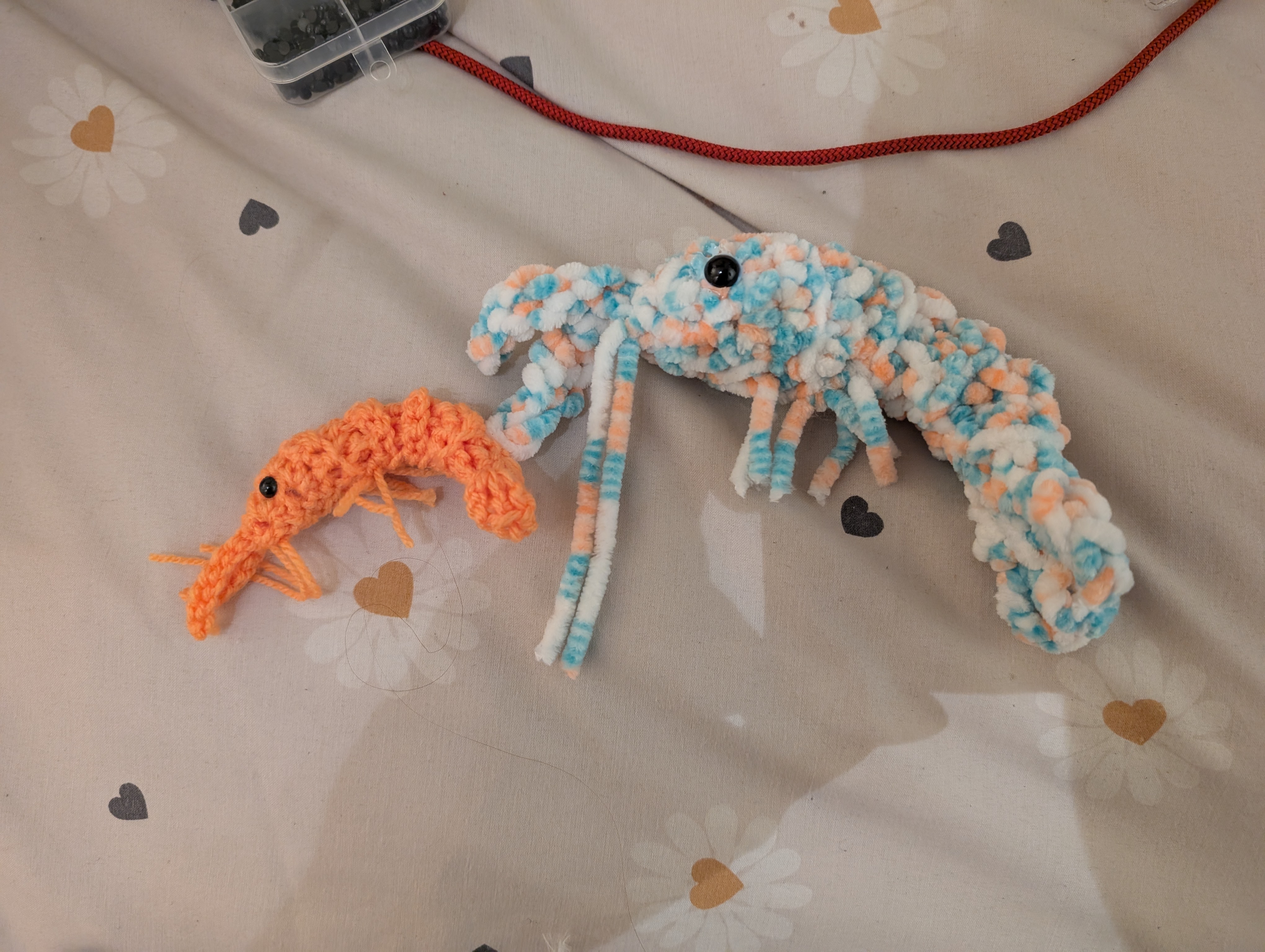 A photo of one small orange crocheted shrimp, and one large fluffy 
crocheted shrimp in pink, blue and 
white.