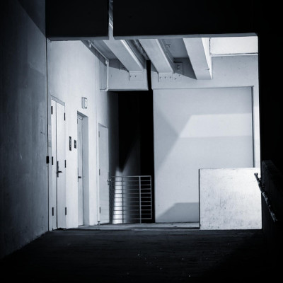 a photo in monochrome of a generic hallway. its fore and back ground are dark and shadowy and its midground is blown out by flourescent lighting